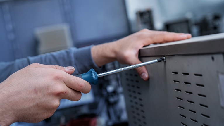 Person using a screwdriver to fasten a screw on a metal enclosure.
