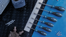 Six screwdrivers arranged by size on a blue work surface next to metal bolts.