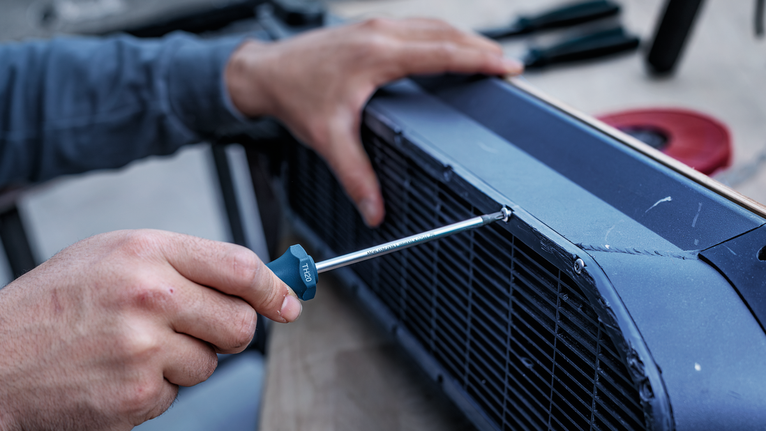 Person using a screwdriver to tighten a screw on a metal panel.