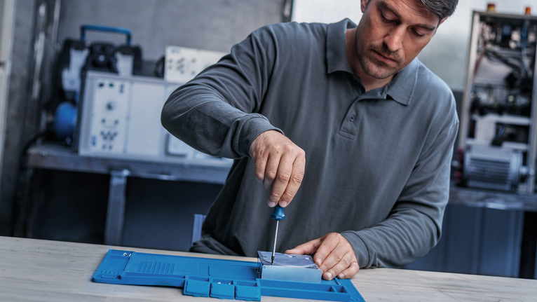 Person assembles a metal component with a screwdriver at a workbench.