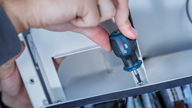 Person using a screwdriver to tighten a screw inside a metal frame.