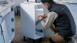 Person wearing safety equipment installs drawer slides inside a cabinet.