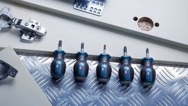 Five stubby screwdrivers lined up on a metal surface near cabinet hardware.
