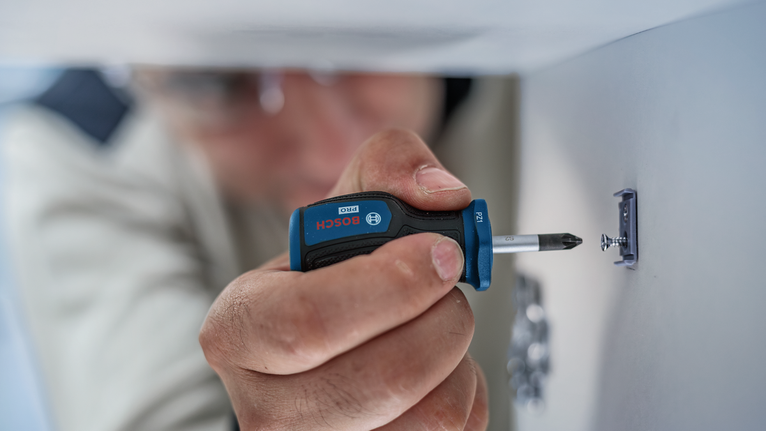 Person fastening a screw into a wall with a manual screwdriver.