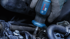 Person wearing safety equipment uses a power screwdriver to tighten a bolt on machinery.