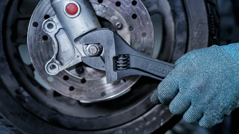 Person wearing safety equipment tightens a bolt on a motorcycle wheel with a wrench.