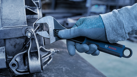 Person wearing safety equipment uses an adjustable wrench to tighten a bolt on machinery.