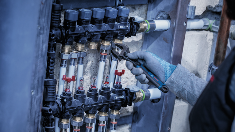 Person wearing safety equipment tightens a pipe fitting with a wrench.