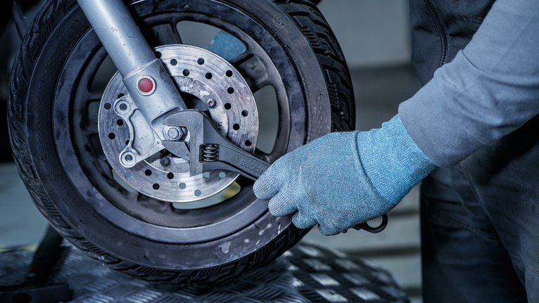 Person wearing safety equipment tightens a bolt on a motorcycle wheel with a wrench.