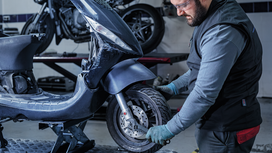 Person wearing safety equipment tightens bolts on a scooter wheel in a workshop.