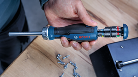 Person holding a screwdriver with multiple bits over a wooden workbench.