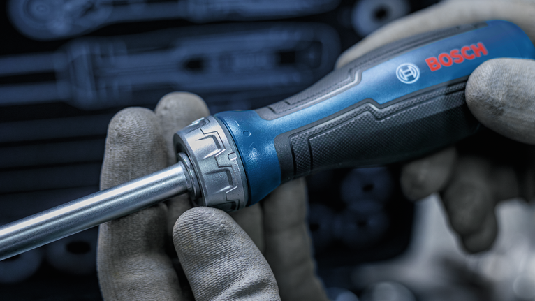 Person wearing safety equipment holds a blue and black screwdriver.