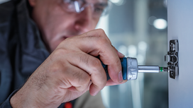 Person wearing safety equipment using a power screwdriver to fasten a hinge on a cabinet.