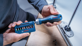 Person loads a screwdriver with a bit from a set near a metal rail.