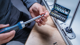 Person attaches a screwdriver bit to a tool near a set of bits on a workbench.