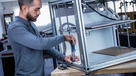 Person using a power screwdriver to assemble a metal frame on a workbench.