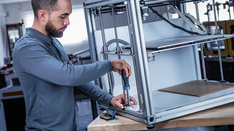 Person using a power screwdriver to assemble a metal frame on a workbench.