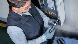Person wearing safety equipment tightens a screw on a control panel with a power screwdriver.