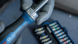 Person wearing safety equipment uses a ratchet screwdriver near a set of bits.