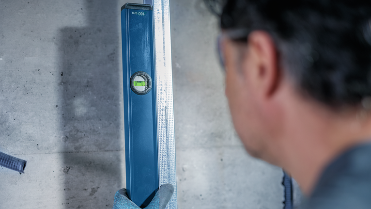 Person wearing safety equipment checks alignment with a spirit level on a concrete wall.