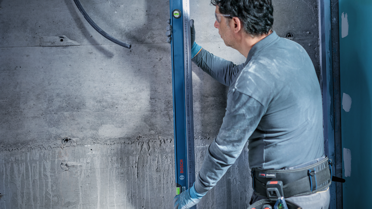 Person wearing safety equipment checks wall alignment with a spirit level.