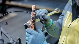 Person wearing safety equipment tightens a metal fitting with a wrench.