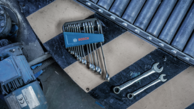 Set of wrenches arranged on a workbench near two loose wrenches and machinery.