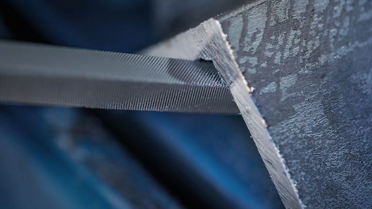 Metal file smoothing the edge of a steel beam.