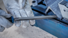 Person wearing safety equipment filing the edge of a metal piece.