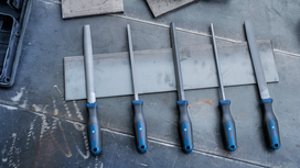 Five metal files with blue and black handles arranged on a metal surface.