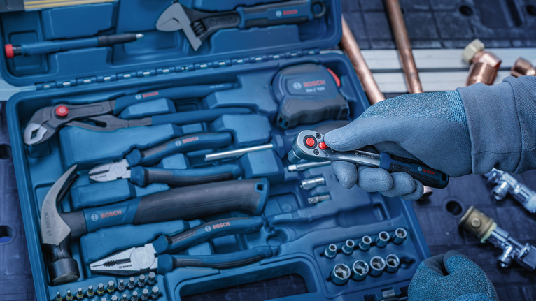 Person wearing safety equipment holds a ratchet in a toolkit with various hand tools.