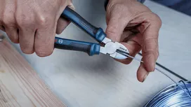 Person cutting metal wire with pliers on a workbench.