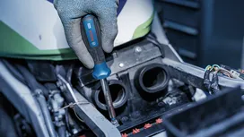 Person wearing safety equipment using a screwdriver to repair a motorcycle engine.