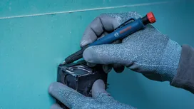 Person wearing safety equipment marks a hole on drywall with a blue marker.