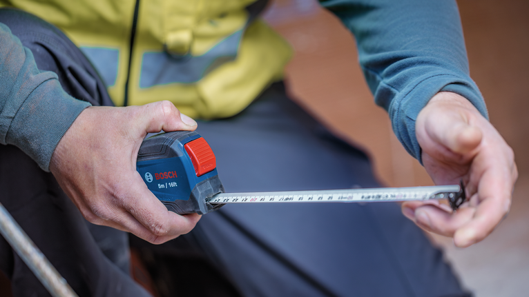 Person wearing safety equipment measures with a tape measure.