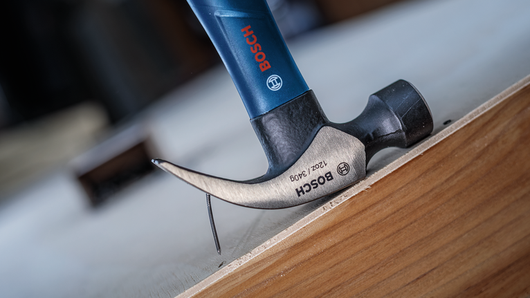 Claw hammer pulling a nail from a wooden board.
