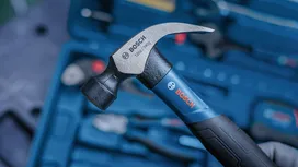 Person holds a claw hammer over a toolbox with assorted tools.