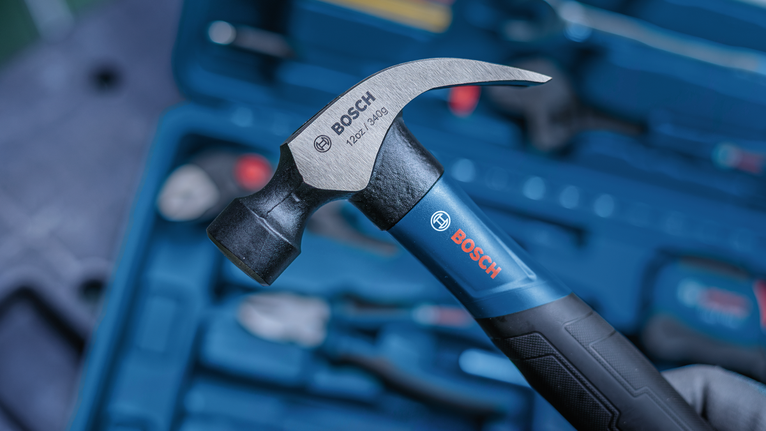 Person holds a claw hammer over a toolbox with assorted tools.