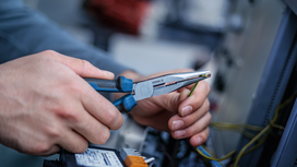 Person holding pliers and stripping electrical wire.