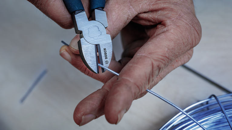 Person uses cutting pliers to trim a metal wire.