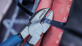 Wire cutter slices through a black cable tie securing red conduit pipes.