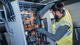 Person wearing safety equipment inspects and adjusts wiring inside an industrial control panel.