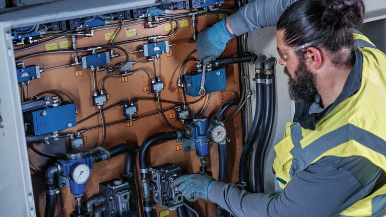 Person wearing safety equipment adjusts valves on complex industrial machinery.