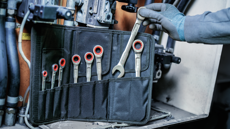 Person wearing safety equipment selects a wrench from a tool roll.