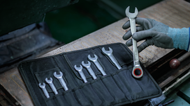 Person wearing safety equipment selects a wrench from a tool roll on a workbench.
