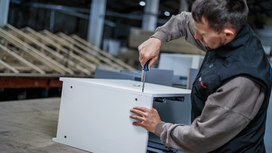Person assembling a cabinet with a power screwdriver in a workshop.