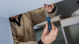 Person fastening a screw under a cabinet with a screwdriver.