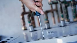 Person using a screwdriver to fasten a screw on a metal surface.