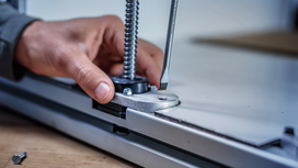 Person fastens a metal clamp on a work surface using a screwdriver.