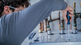 Person wearing safety equipment uses a screwdriver to fasten a panel on metal equipment.